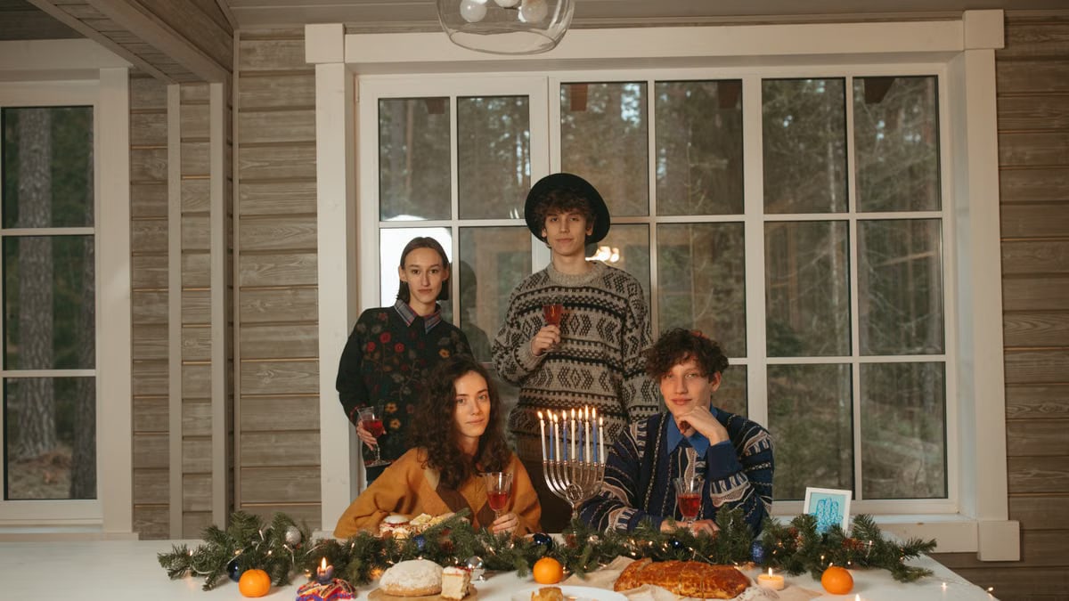 Group of friends celebrating Hanukkah indoors with menorah and decorated table.