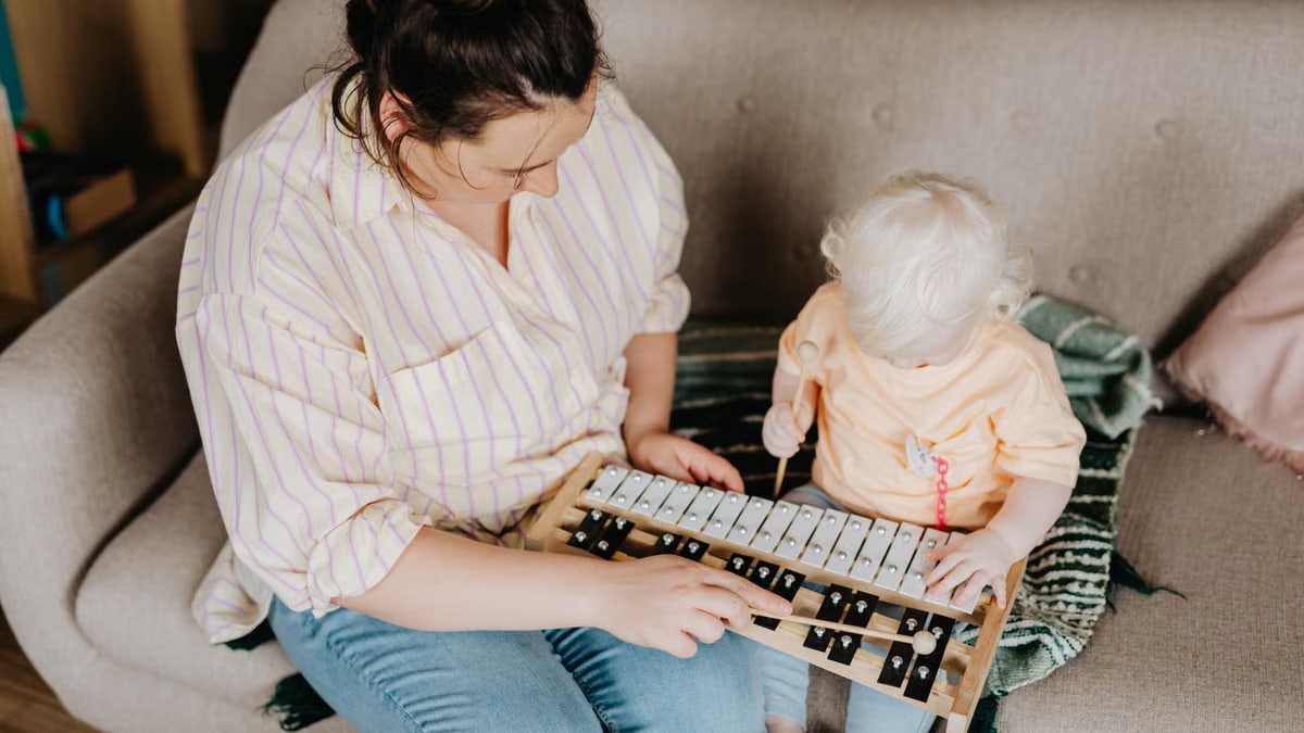A mother and her toddler daughter playing a xylophone together indoors on a cozy sofa.